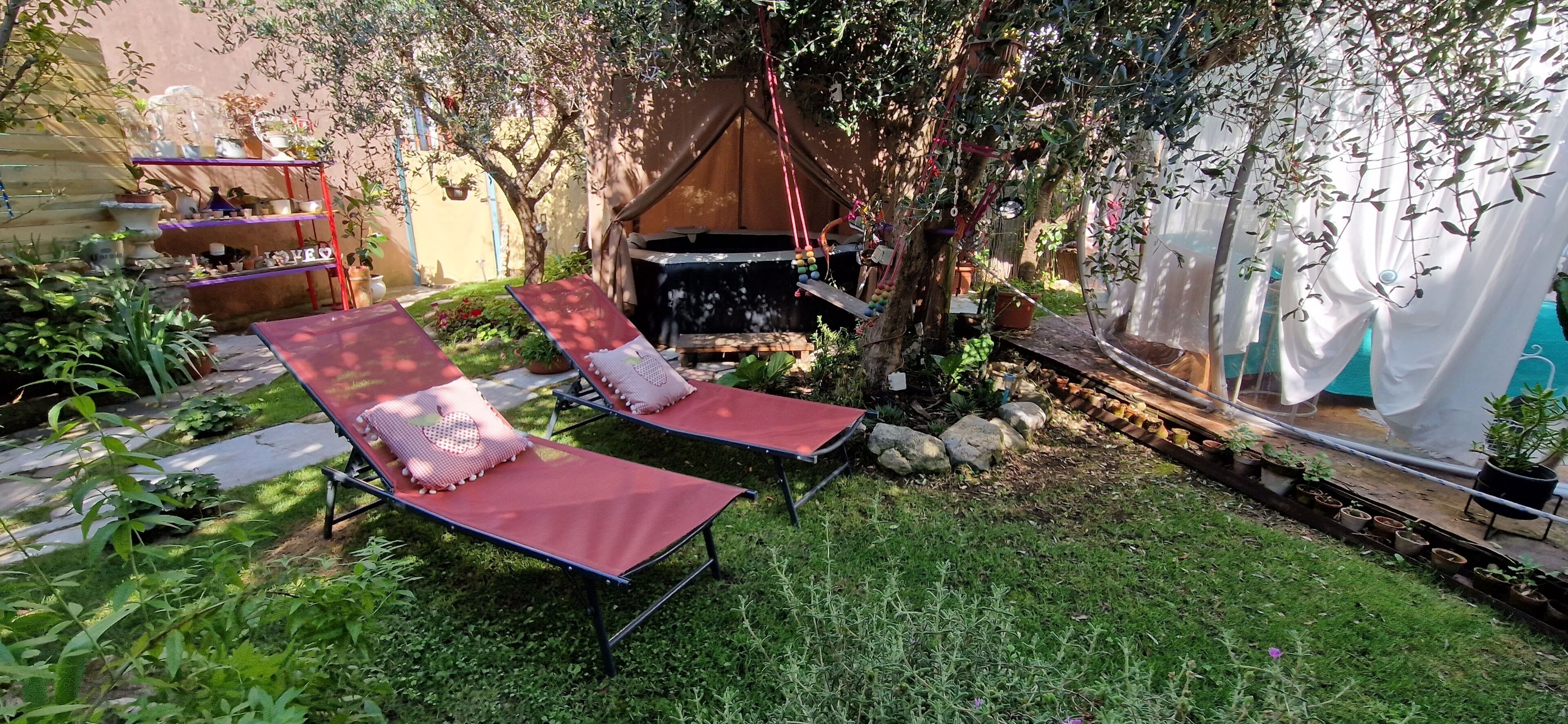Ein Garten mit zwei roten Liegestühlen, einem kleinen Tisch und verschiedenen Topfpflanzen.