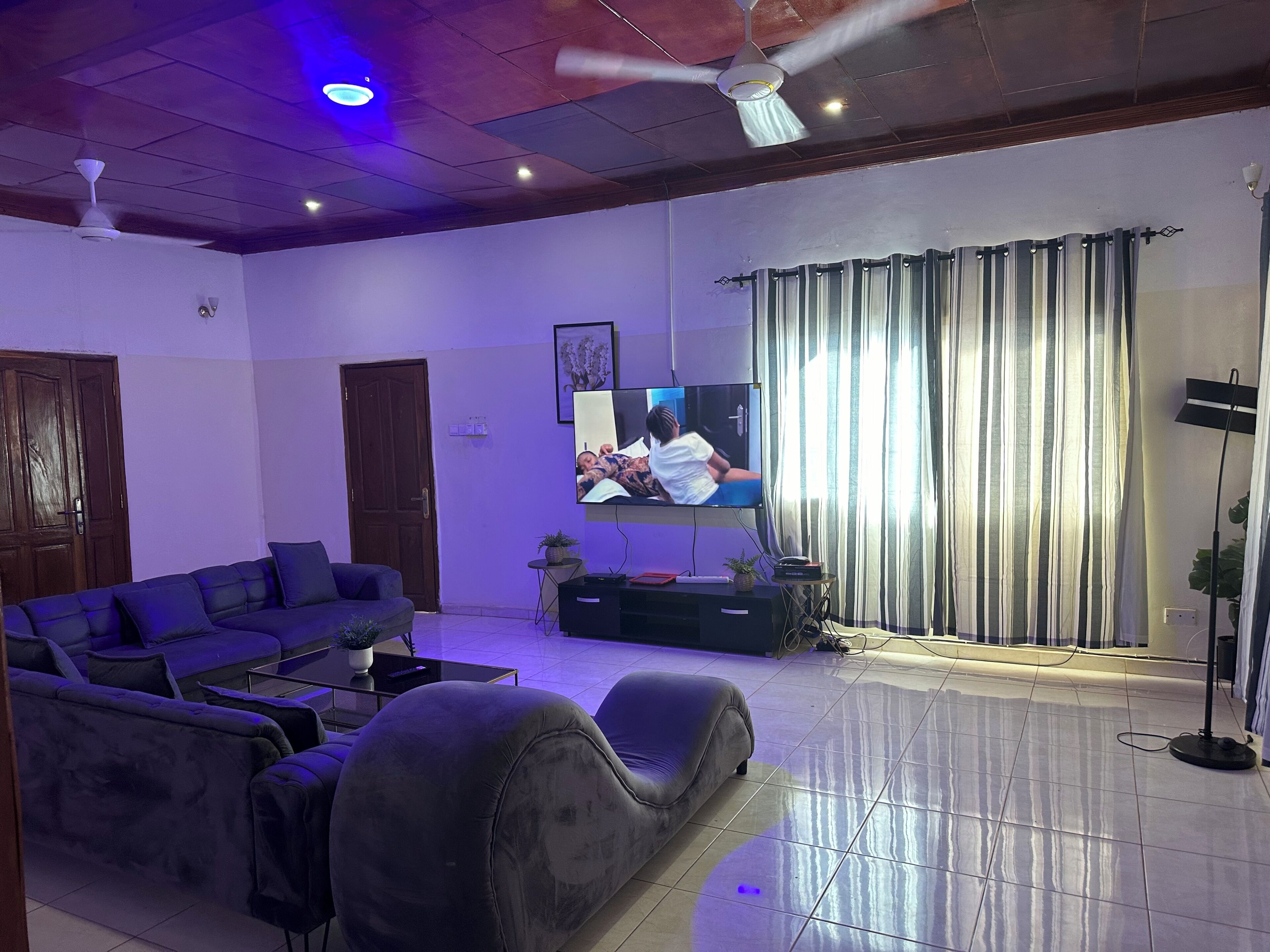 Un salon avec un canapé, une télévision, un ventilateur de plafond et des rideaux.