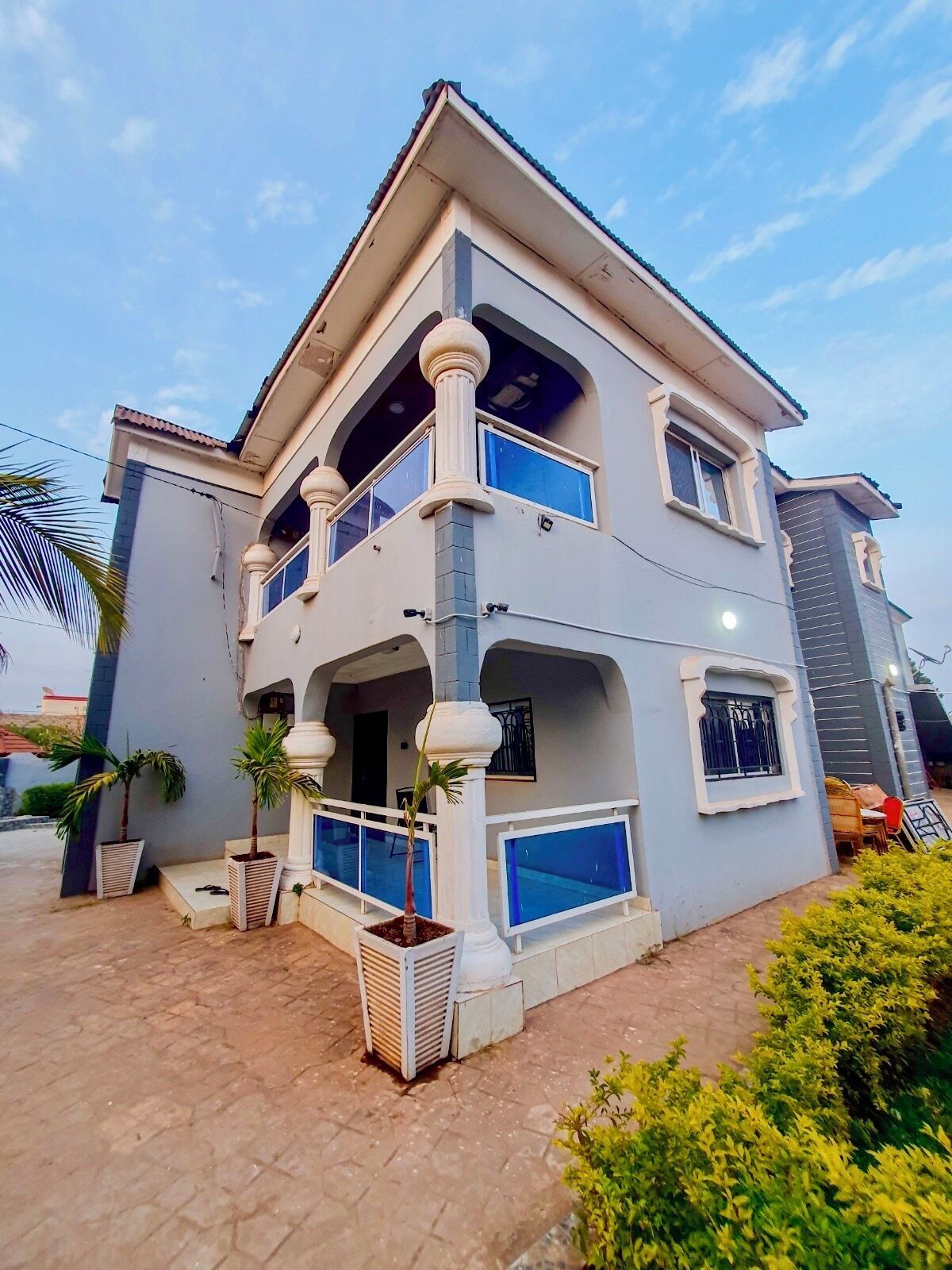A two-story building with a balcony, a covered patio area, and a small garden with potted plants.