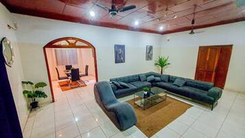 A living room with a sectional sofa, a glass coffee table, and a dining area with chairs and a table.