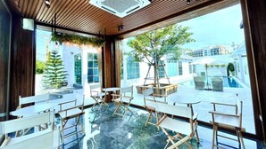 Un espace intérieur moderne doté d’un plancher en verre, d’un plafond en bois et de grandes fenêtres offrant une vue sur une piscine et des bâtiments.