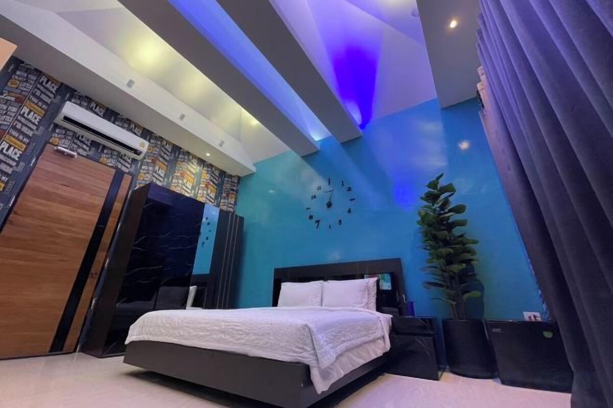 Une chambre à coucher moderne avec un lit, une table de chevet, une plante en pot et une horloge murale.