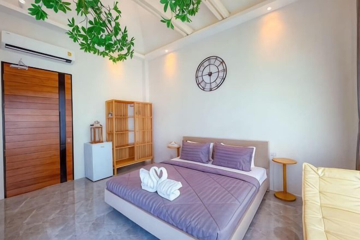 Une chambre moderne avec un grand lit, une armoire, une petite table et un luminaire fixé au mur.