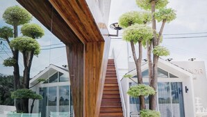 Un bâtiment moderne avec un escalier en bois menant à une porte en verre, le tout entouré d’arbres.