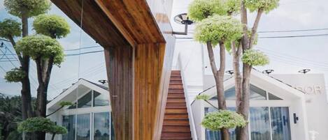Un edificio moderno con una escalera de madera que lleva a una puerta de cristal, rodeado de árboles.