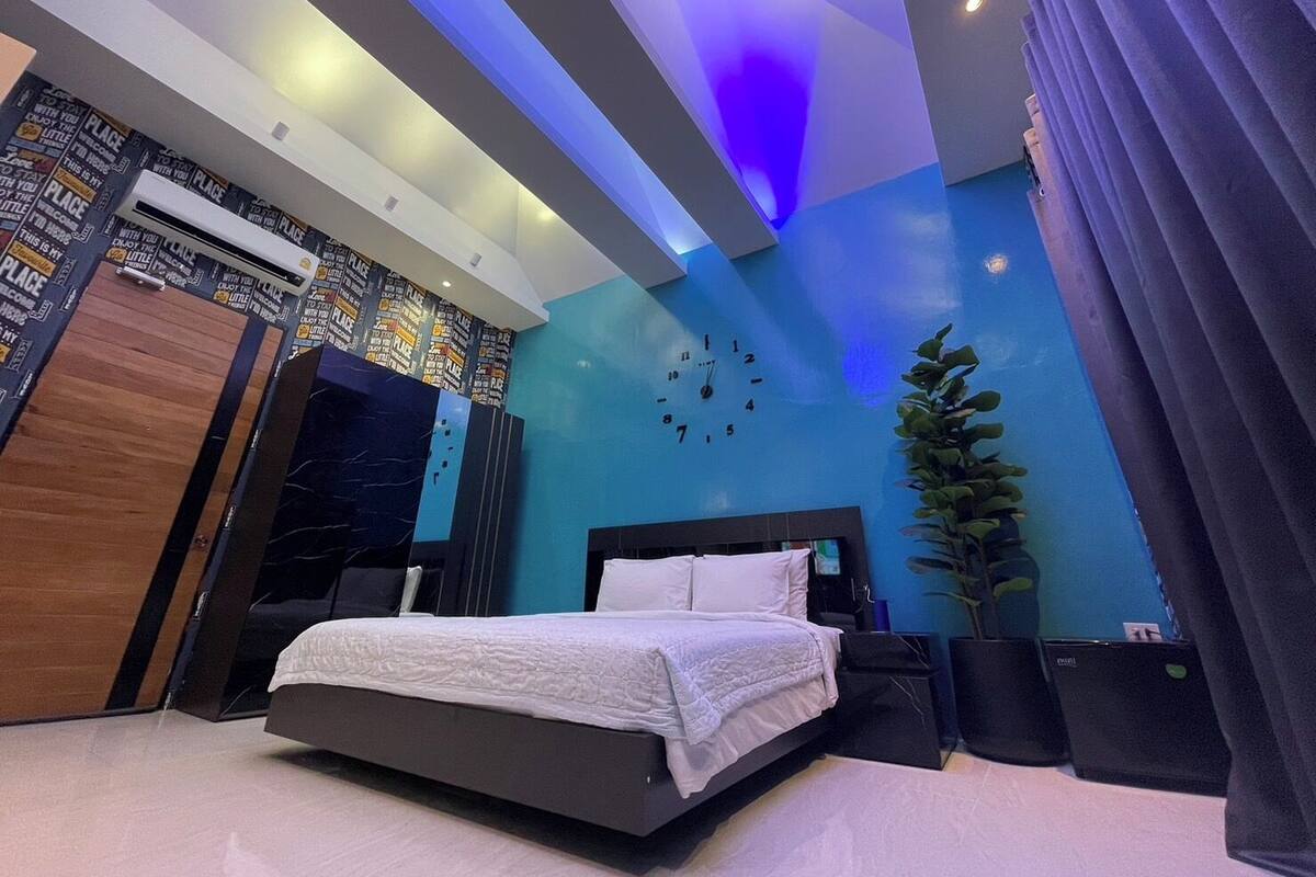 A modern bedroom with a bed, a clock, and a large plant.