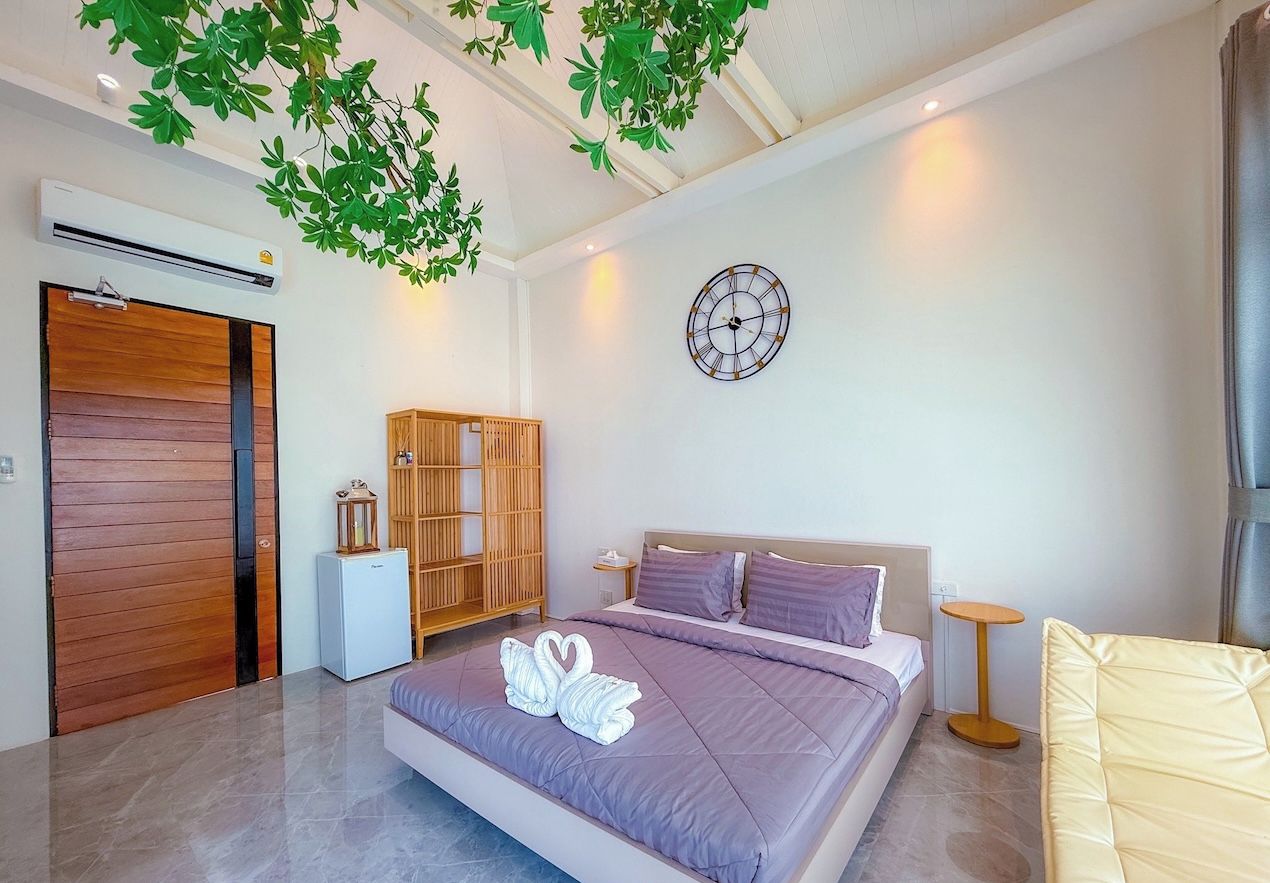 Een moderne slaapkamer met een groot bed, een houten garderobe, een klein tafeltje en een wandklok.