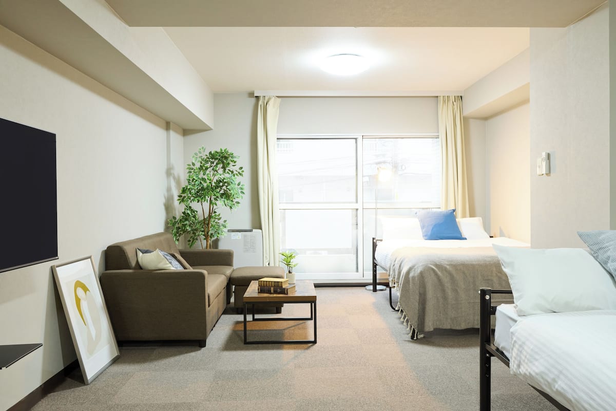 A modern hotel room with a sofa, a bed, a small table, a TV, and a large window with curtains.