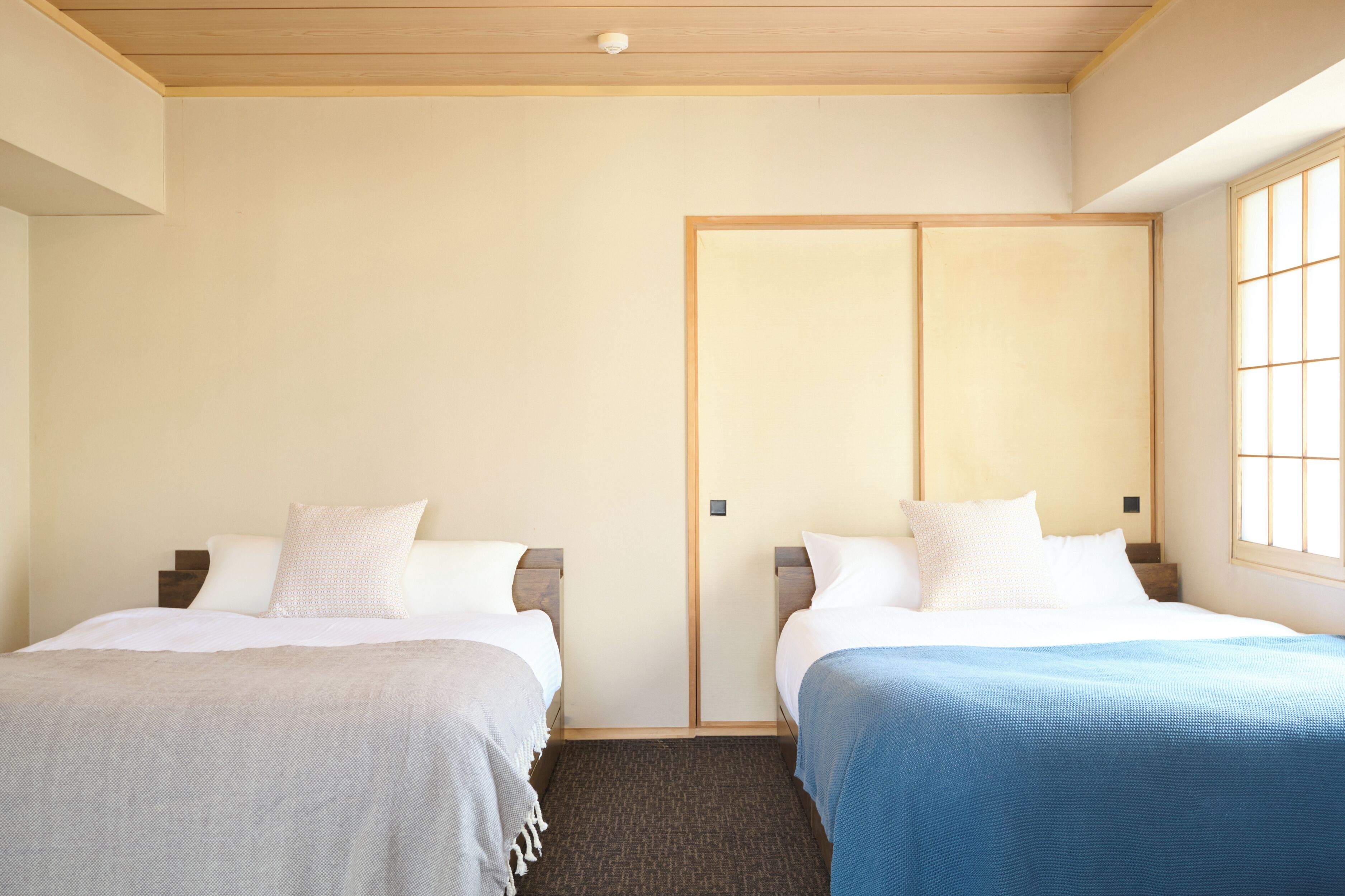 A hotel room with two beds, a wooden ceiling, and a sliding door.