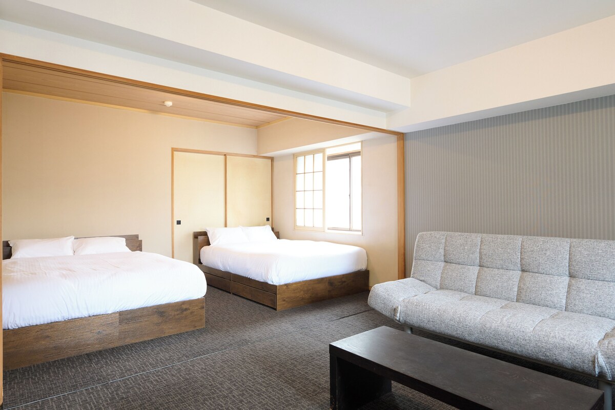 Una habitación de hotel con dos camas, un sofá, una mesita y un ventanal.