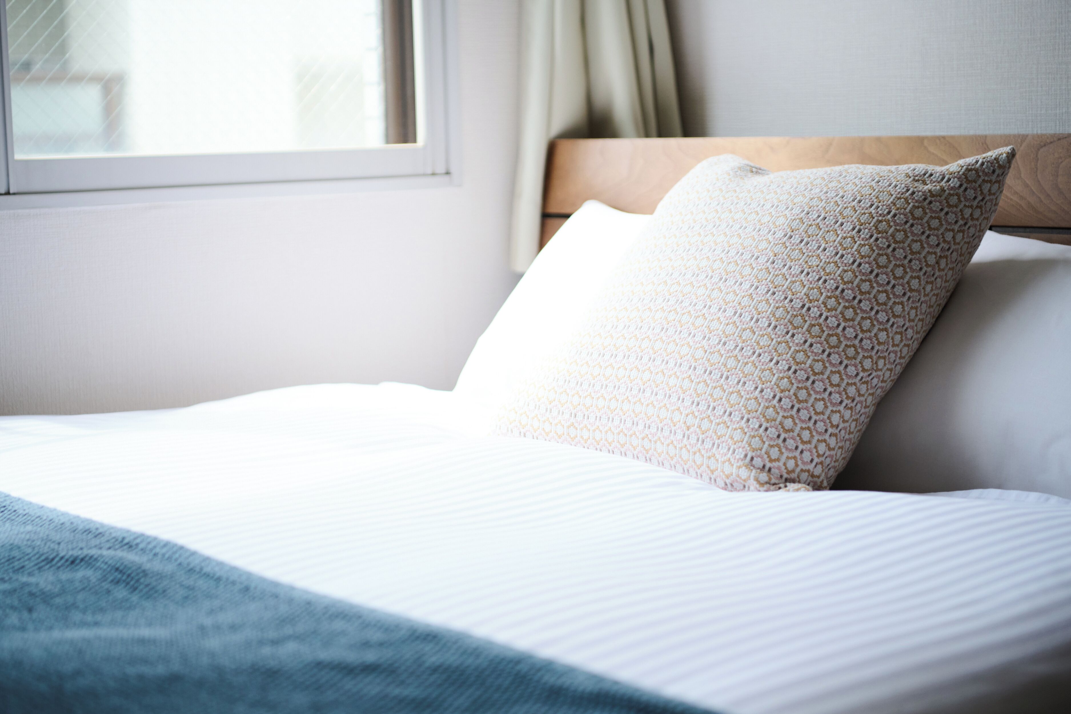 A neatly made bed with a patterned pillow and a blue throw blanket.