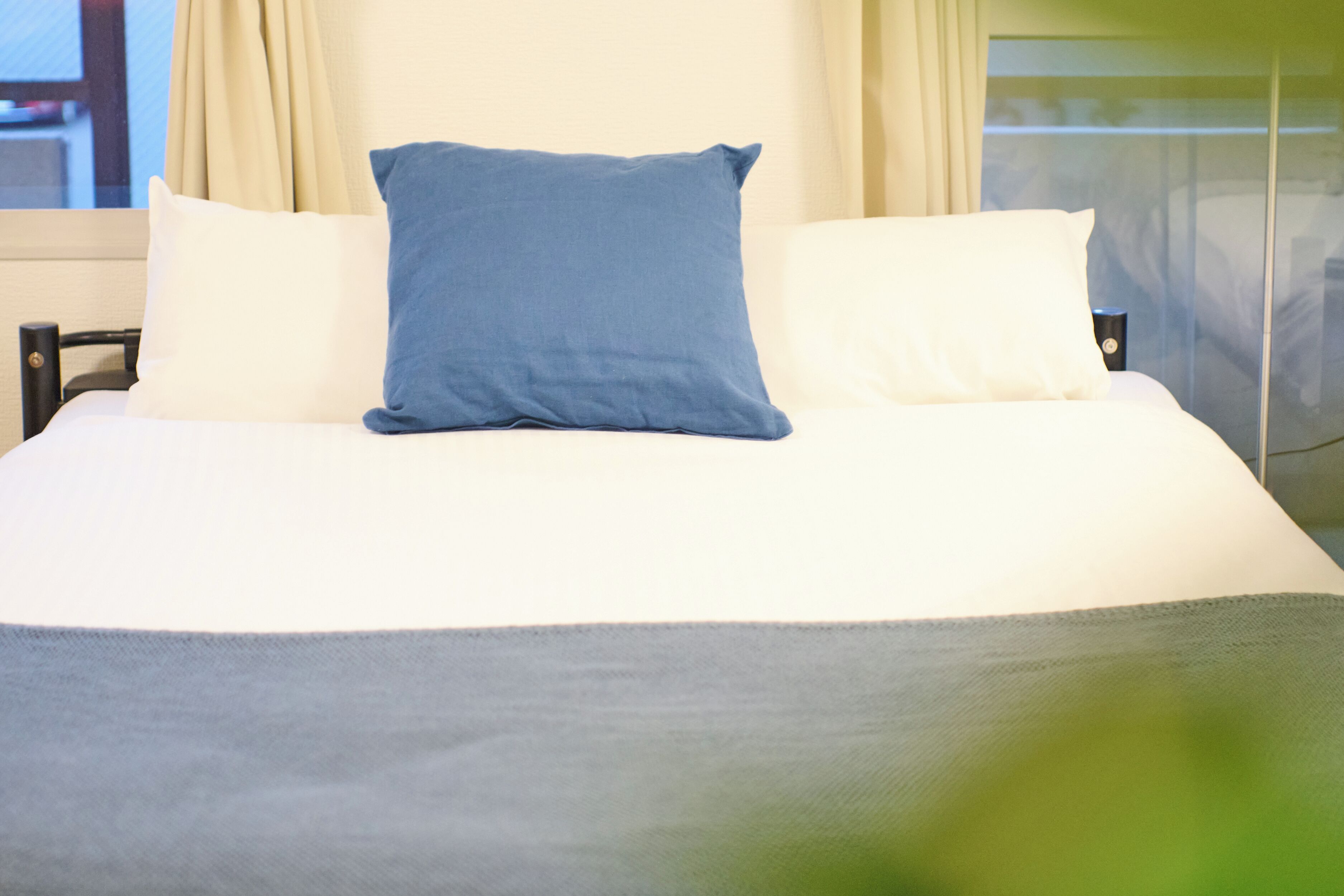 Un letto con cuscini bianchi e azzurri, una coperta grigia e una finestra con tende.