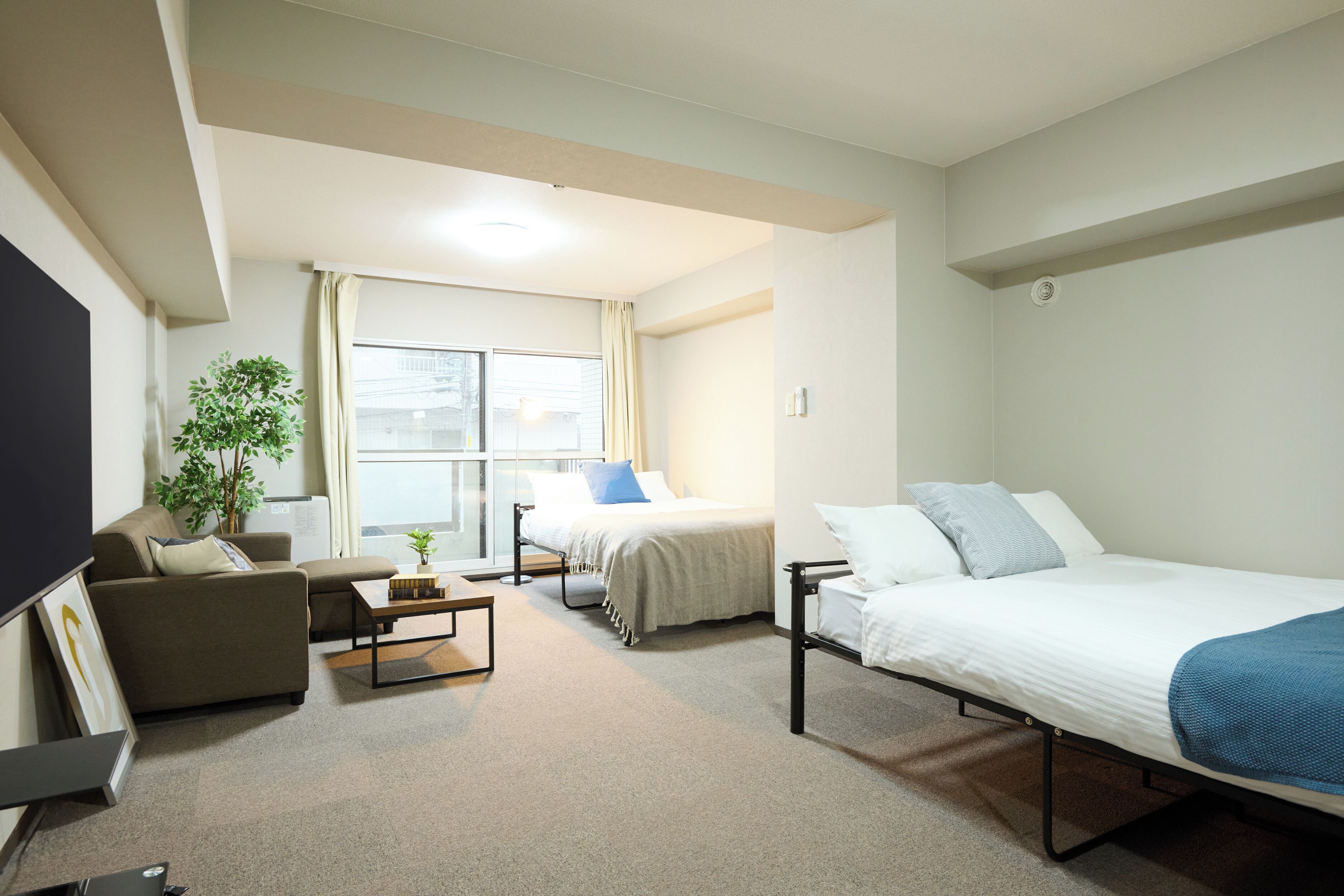 A modern hotel room with a sofa, a bed, a desk, and a large window.