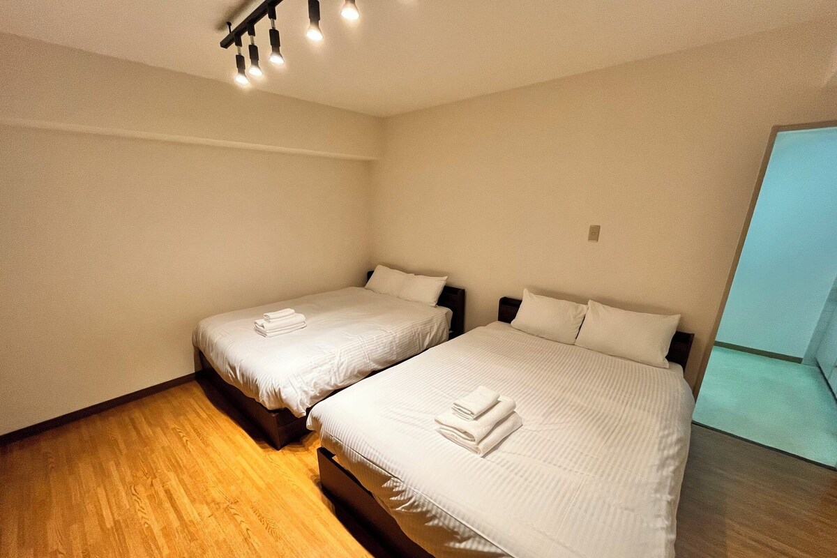 Habitación de hotel con dos camas, piso de madera y una lámpara en el techo.