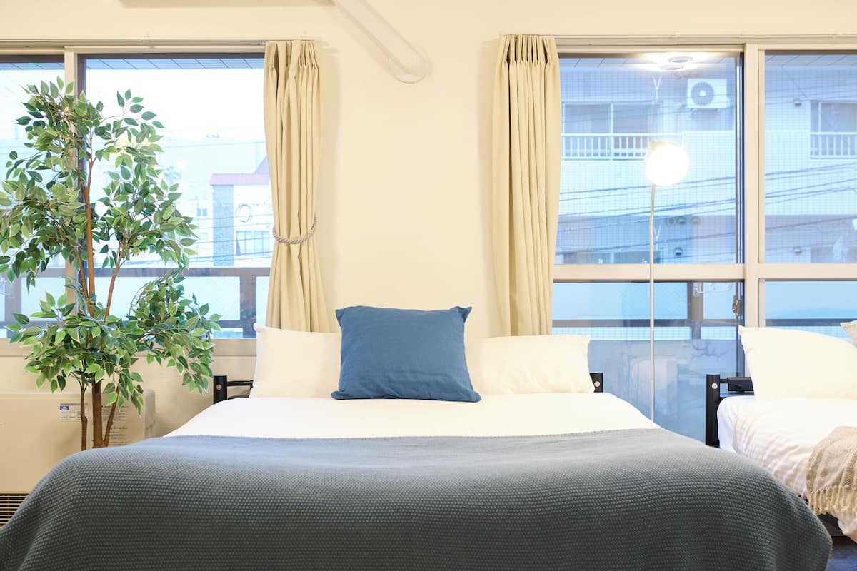 A hotel room with a bed, a potted plant, and a view of buildings through the window.