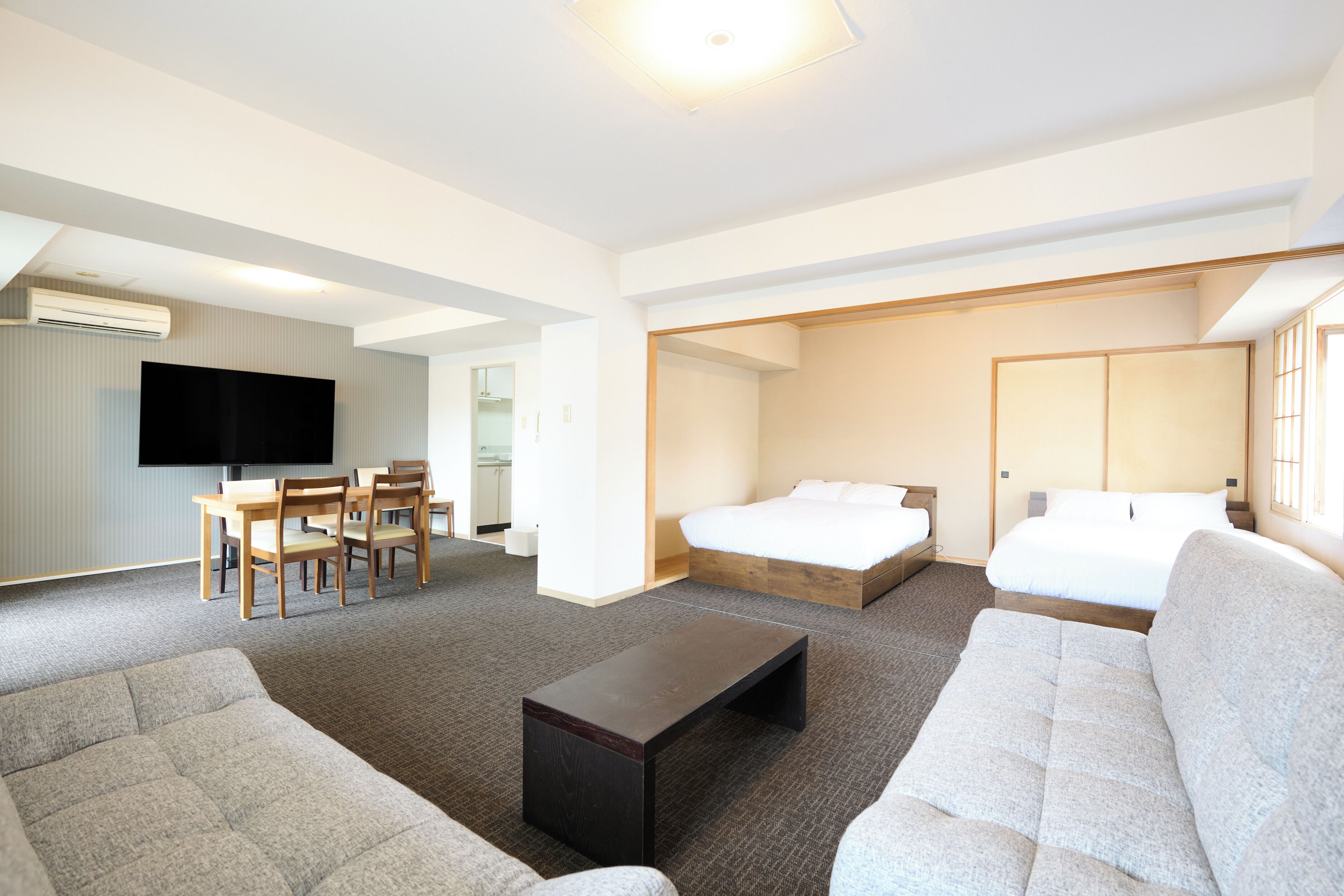 A hotel room with a bed, sofa, TV, and a dining area with chairs.
