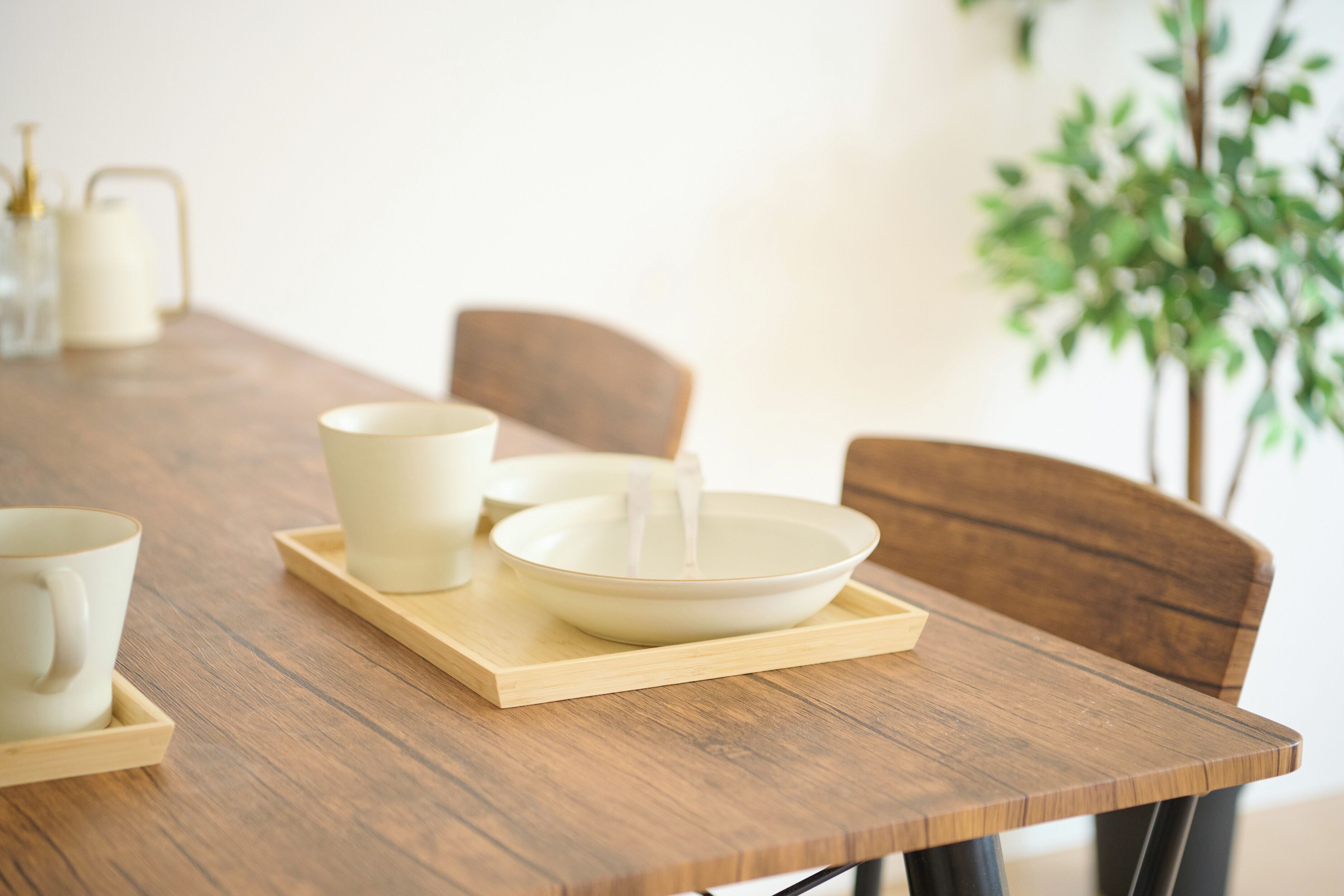 A wooden dining table with a bowl and two cups on a tray.