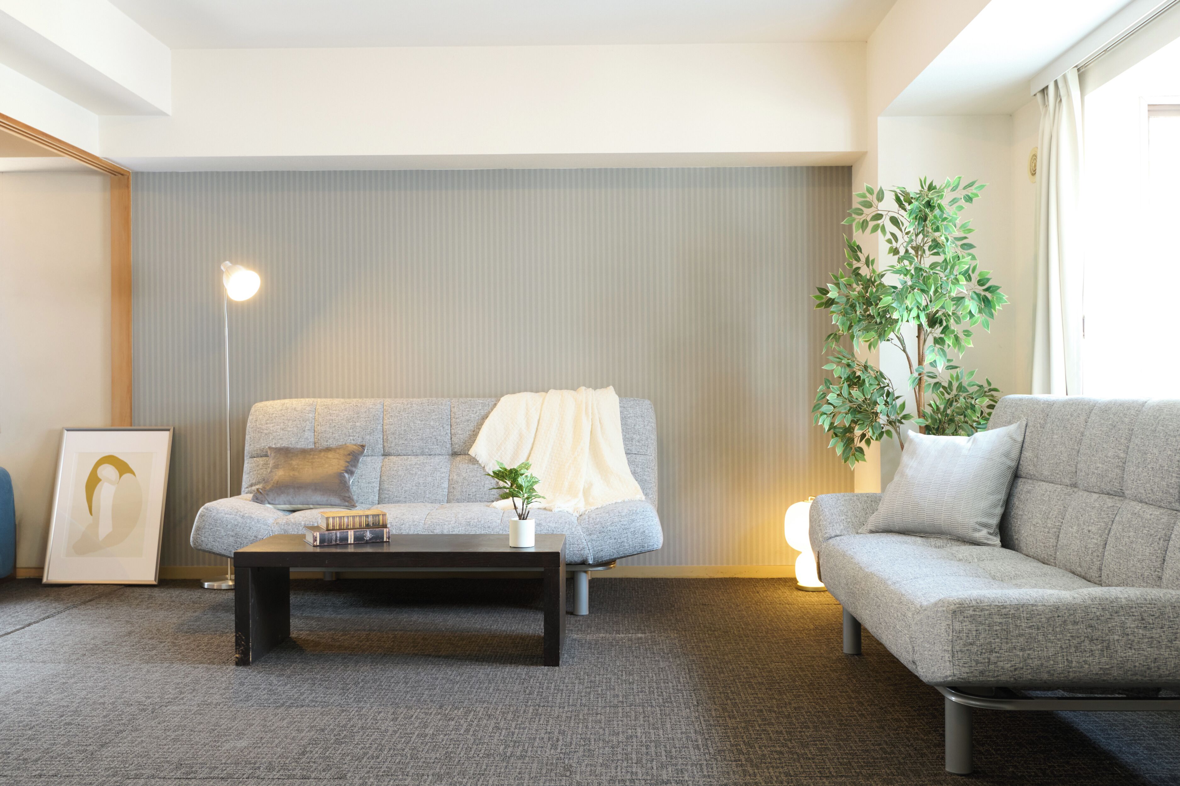 Una sala de estar moderna con un sofá gris, una mesa de centro oscura y una planta grande en maceta.