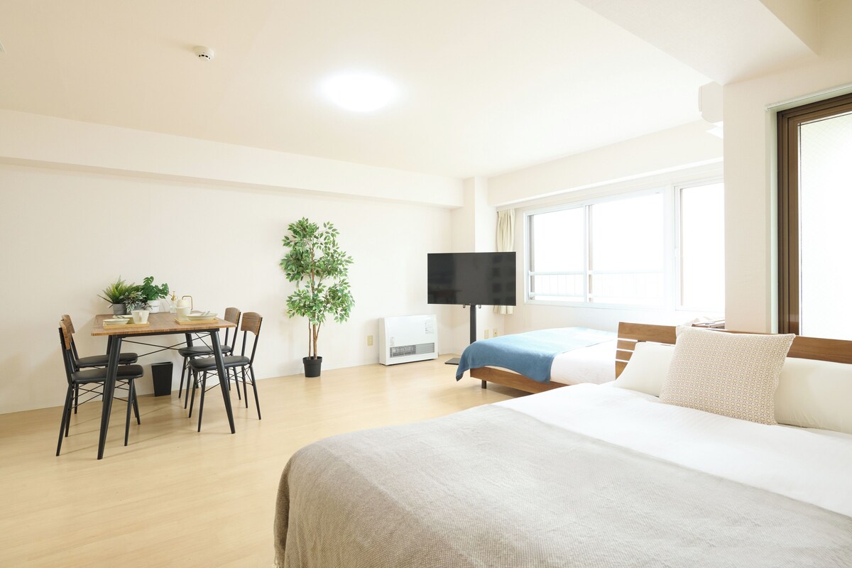 Habitación de hotel con cama, televisor, mesa de comedor con sillas y una planta en maceta.