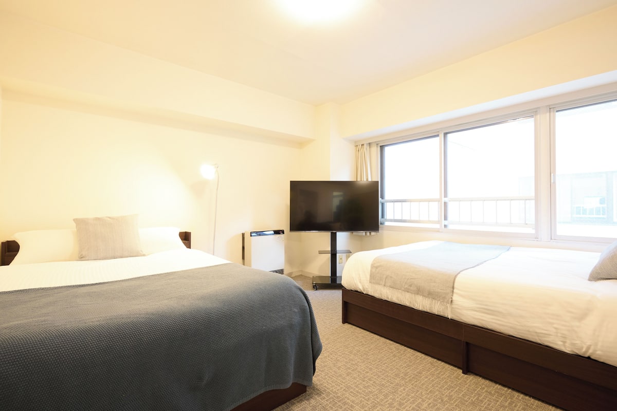 A hotel room with two beds, a TV, and a window with a view.