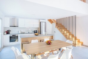 A modern kitchen with white cabinets, a wooden dining table, and a staircase with wooden steps and metal railings.