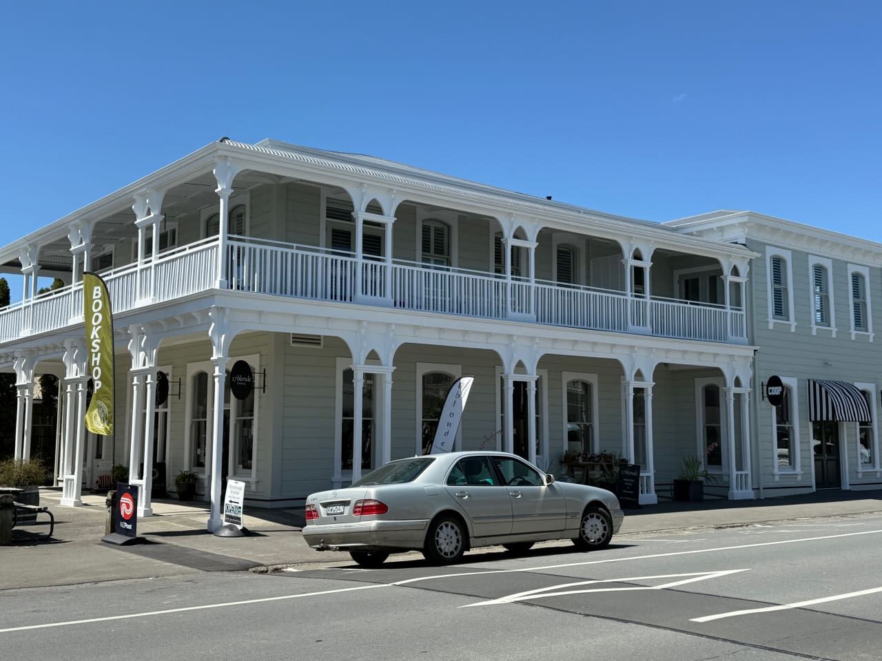 A two-story building with a balcony on the upper floor, a sign that reads 'BOOKSHOP,' and a parked car in front.