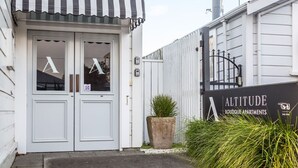 A boutique apartment building entrance with a striped awning, a large planter, and a sign for 'Altitude Boutique Apartments'. - Altitude Apartment Stylish Village Apartment | 2BR, Balcony & Prime Location (Martinborough)