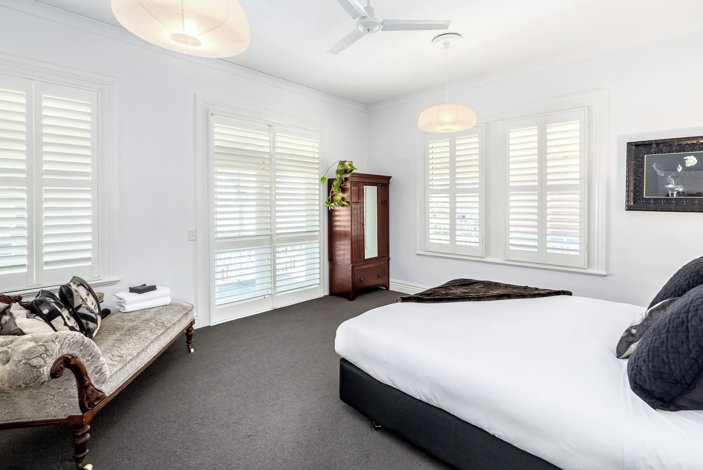 Une chambre à coucher avec un lit, un banc, une armoire et un ventilateur de plafond.