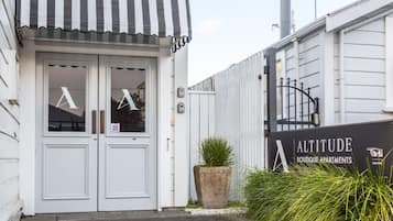Entrada a un apartamento boutique con un toldo a rayas, una planta grande en maceta y un cartel que dice 'ALTITUDE Boutique Apartments'.