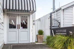 A boutique apartment entrance with a striped awning, a large potted plant, and a sign for 'ALTITUDE Boutique Apartments'.
