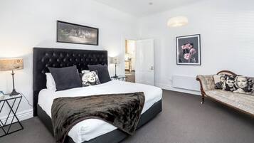 A hotel room with a large bed, a sofa, a desk, and a mirror.