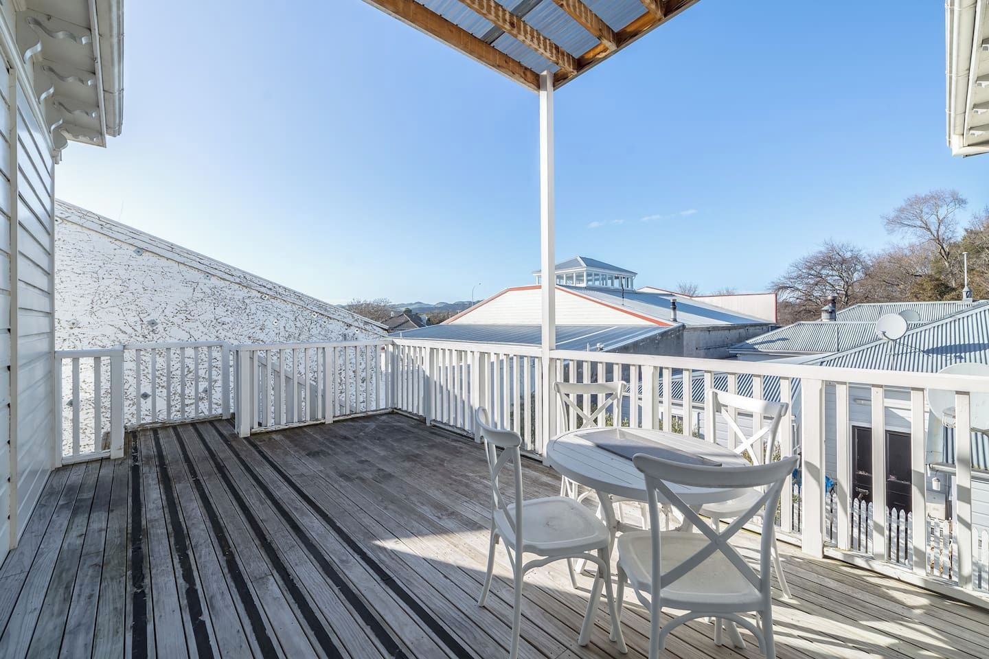A covered outdoor deck with a white railing, a table, and two chairs.