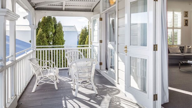 A covered porch with white wicker chairs, a view of the ocean, and a glimpse of the interior. - Altitude Apartment Stylish Village Apartment | 2BR, Balcony & Prime Location (Martinborough)
