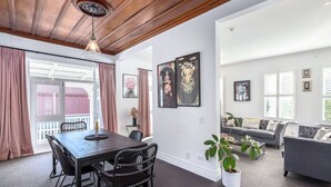 A spacious living area with a dark wooden dining table, black chairs, a grey sofa, and a potted plant. - Altitude Apartment Stylish Village Apartment | 2BR, Balcony & Prime Location (Martinborough)