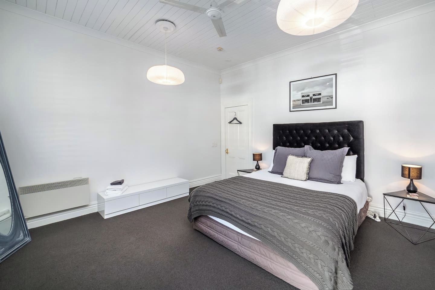 Une chambre à coucher moderne avec un grand lit, des lampes de chevet, un luminaire suspendu et un tableau encadré au mur.
