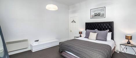 Una camera da letto moderna con un letto grande, abat-jour, una lampada a sospensione e un quadro incorniciato al muro.