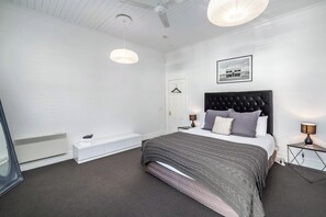 A modern bedroom with a large bed, bedside lamps, a hanging light fixture, and a framed picture on the wall.