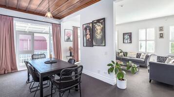 Una sala de estar moderna con comedor, que incluye una mesa de madera oscura, sillas de mimbre, un sofá gris y una planta en maceta.