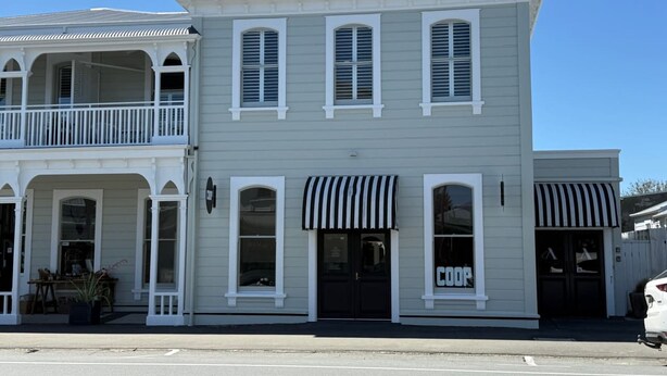 A two-story building with a balcony on the upper level, a storefront with a striped awning, and a sign that reads 'COOP'. - Altitude Studio Apartment (Martinborough)