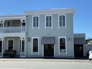A two-story building with a balcony on the upper level, a storefront with a striped awning, and a sign that reads 'COOP'. - Altitude Studio Apartment (Martinborough)