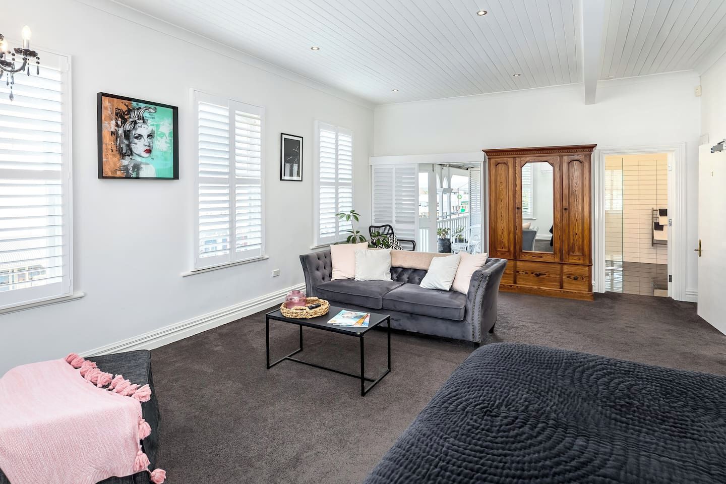 A spacious living room with a grey sofa, a coffee table, and a large window with blinds.