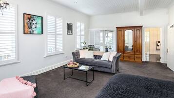 A spacious living room with a grey sofa, a coffee table, and a large window with blinds.