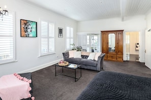 A spacious living room with a grey sofa, a coffee table, and a large window with blinds. - Altitude Studio Apartment (Martinborough)