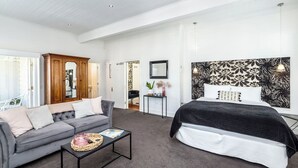 A modern bedroom with a grey sofa, a bed with a black headboard, and a small bedside table. - Altitude Studio Apartment (Martinborough)