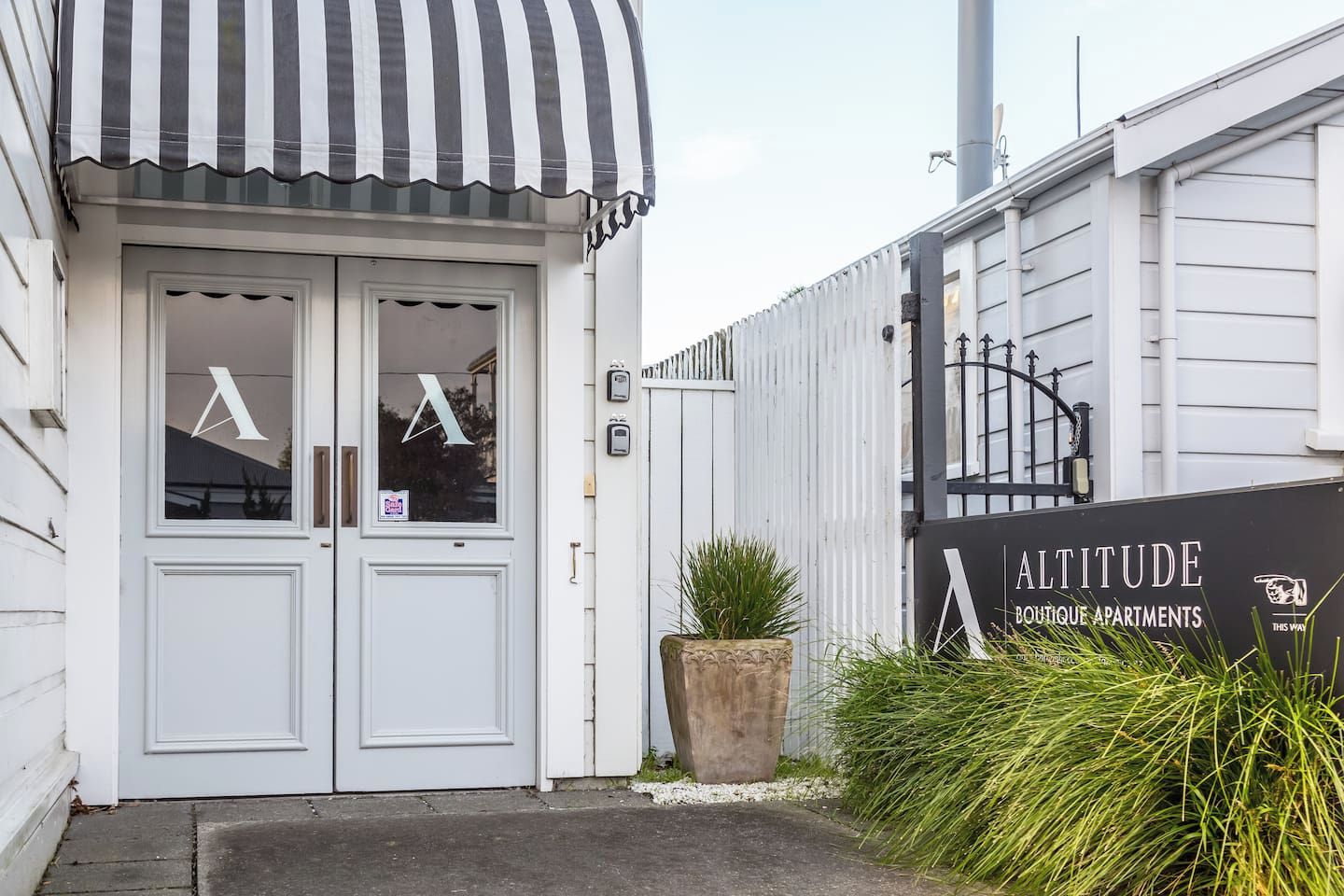 A boutique apartment building entrance with a striped awning, a large potted plant, and a sign for 'Altitude Boutique Apartments'.