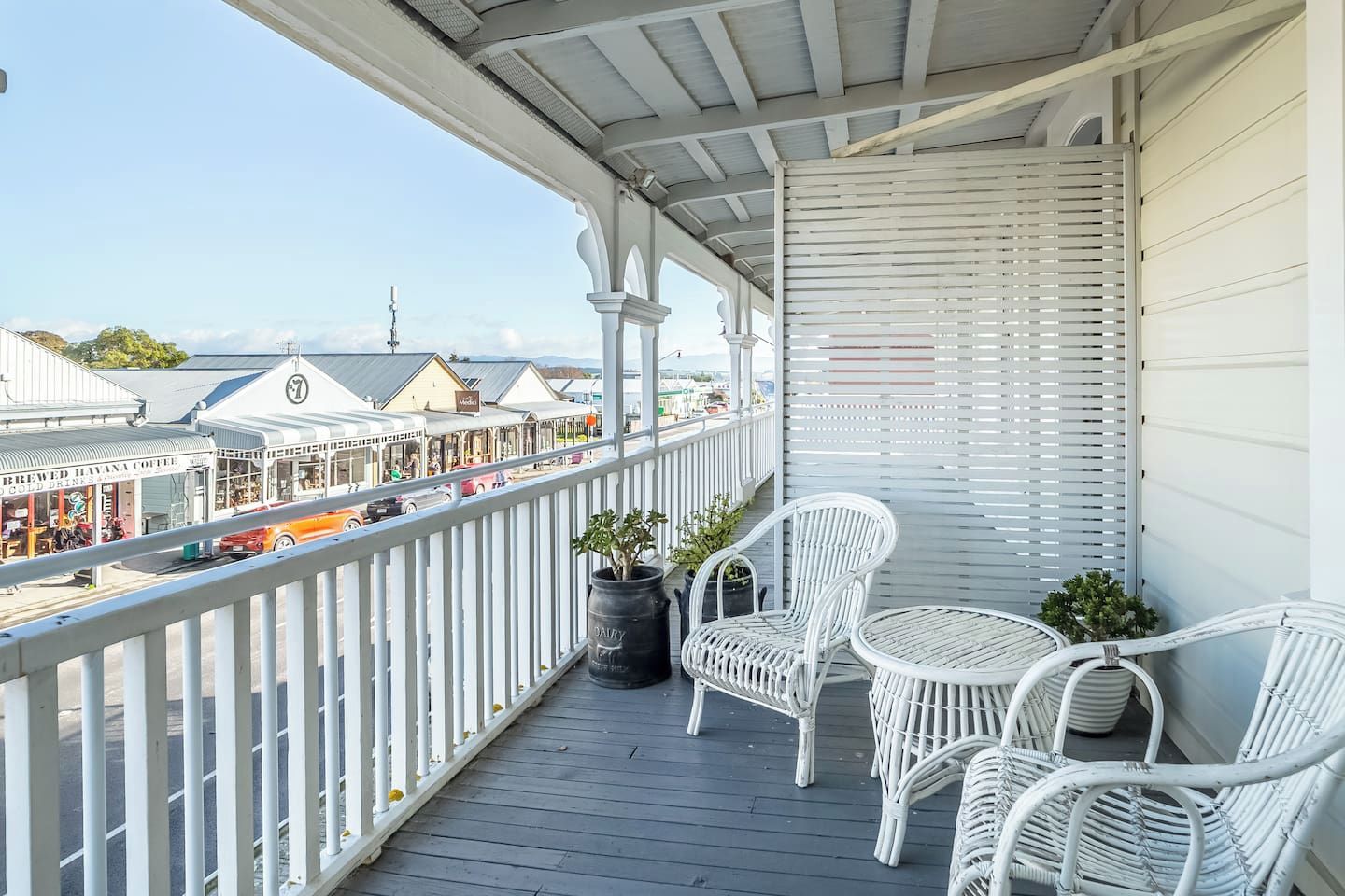 En balkon med hvide fletstole og en potteplante.