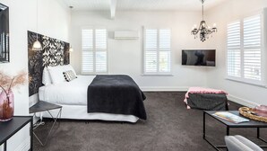 A bedroom with a bed, bedside tables, a TV, and a chandelier. - Altitude Studio Apartment (Martinborough)