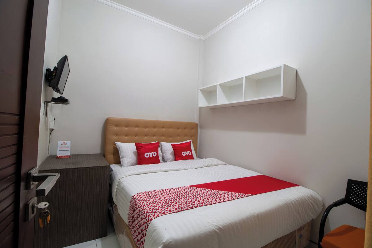 Ein ordentlich eingerichtetes Hotelzimmer mit Bett, Nachttisch, Stuhl und Regalelement.