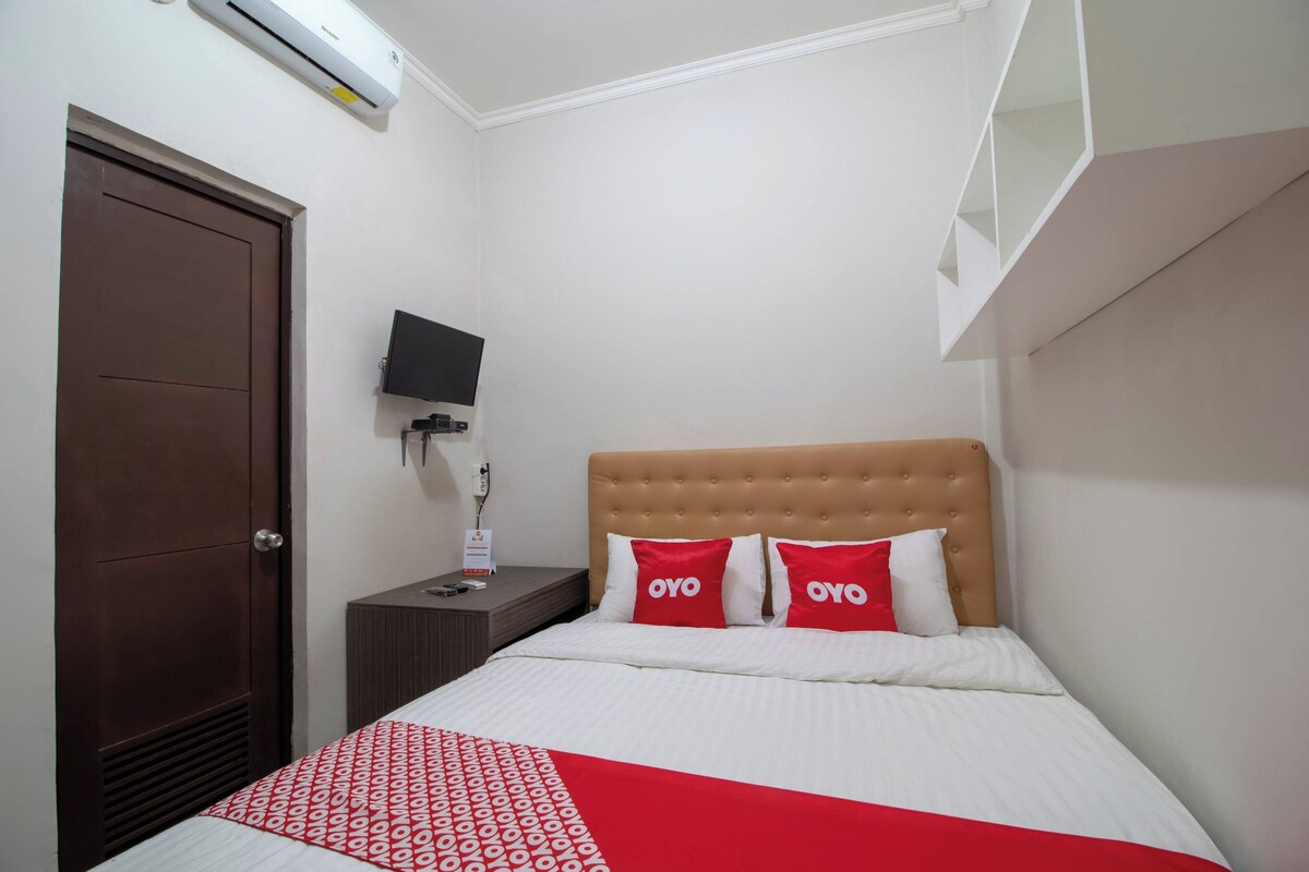 A hotel room with a bed, a television on a nightstand, a door, and an air conditioning unit.