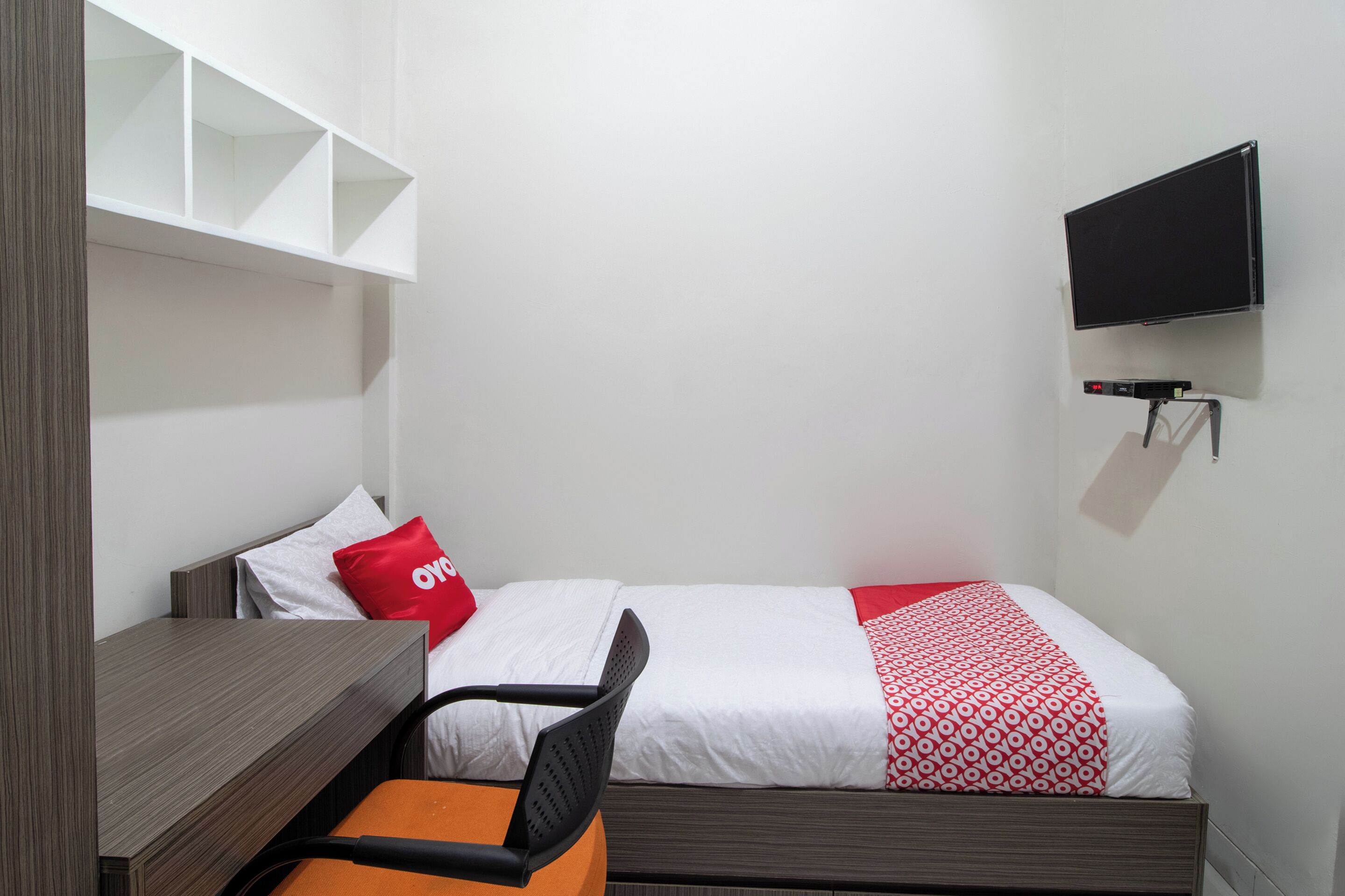 Une petite pièce, bien rangée, avec un lit, un bureau, une chaise et un téléviseur fixé au mur.